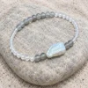 Pale Orbit moonstone and baroque pearl bracelet resting on a smooth pale stone