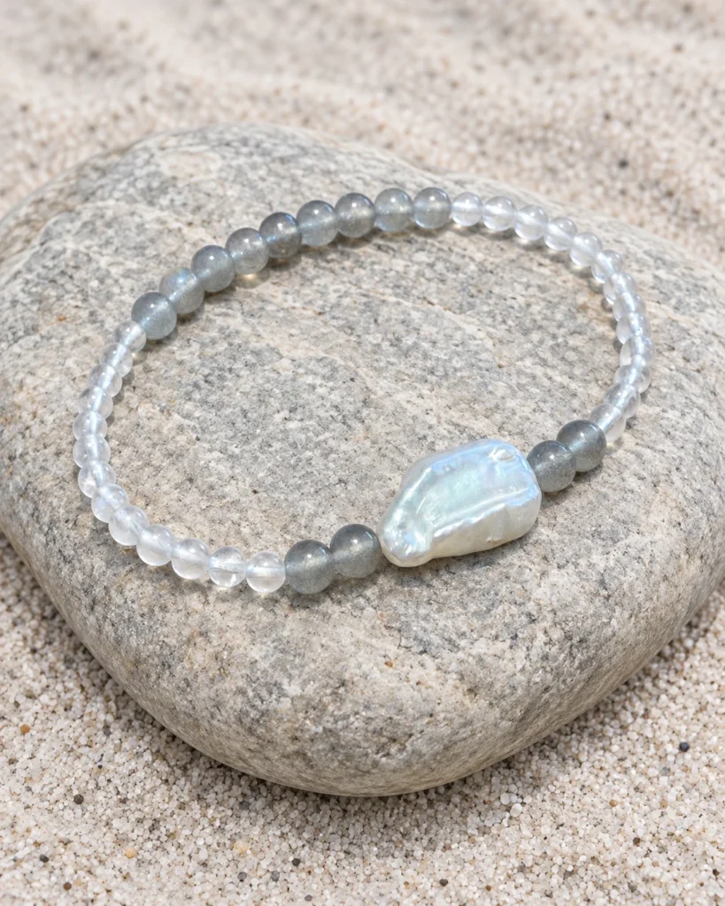 Pale Orbit moonstone and baroque pearl bracelet resting on a smooth pale stone