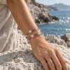 Close-up of Quiet Orbit quartz and moonstone beads arranged in two rows on a wrist beside coastal rocks
