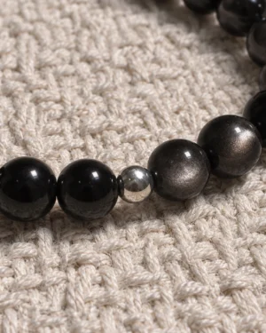 Close-up of Silver Nocturne obsidian, silver sheen obsidian and a sterling silver accent on woven fabric