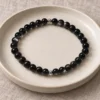 Silver Nocturne obsidian bracelet with two silver accents on a ceramic plate and linen