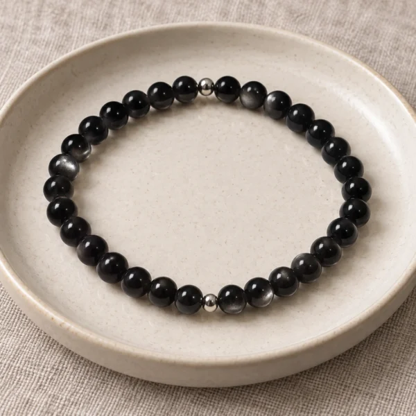 Silver Nocturne obsidian bracelet with two silver accents on a ceramic plate and linen