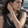 Model wearing the Tidal Glass green fluorite bracelet near her chin beside coastal rocks