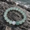 Tidal Glass green fluorite bracelet resting on a dark coastal rock beside water