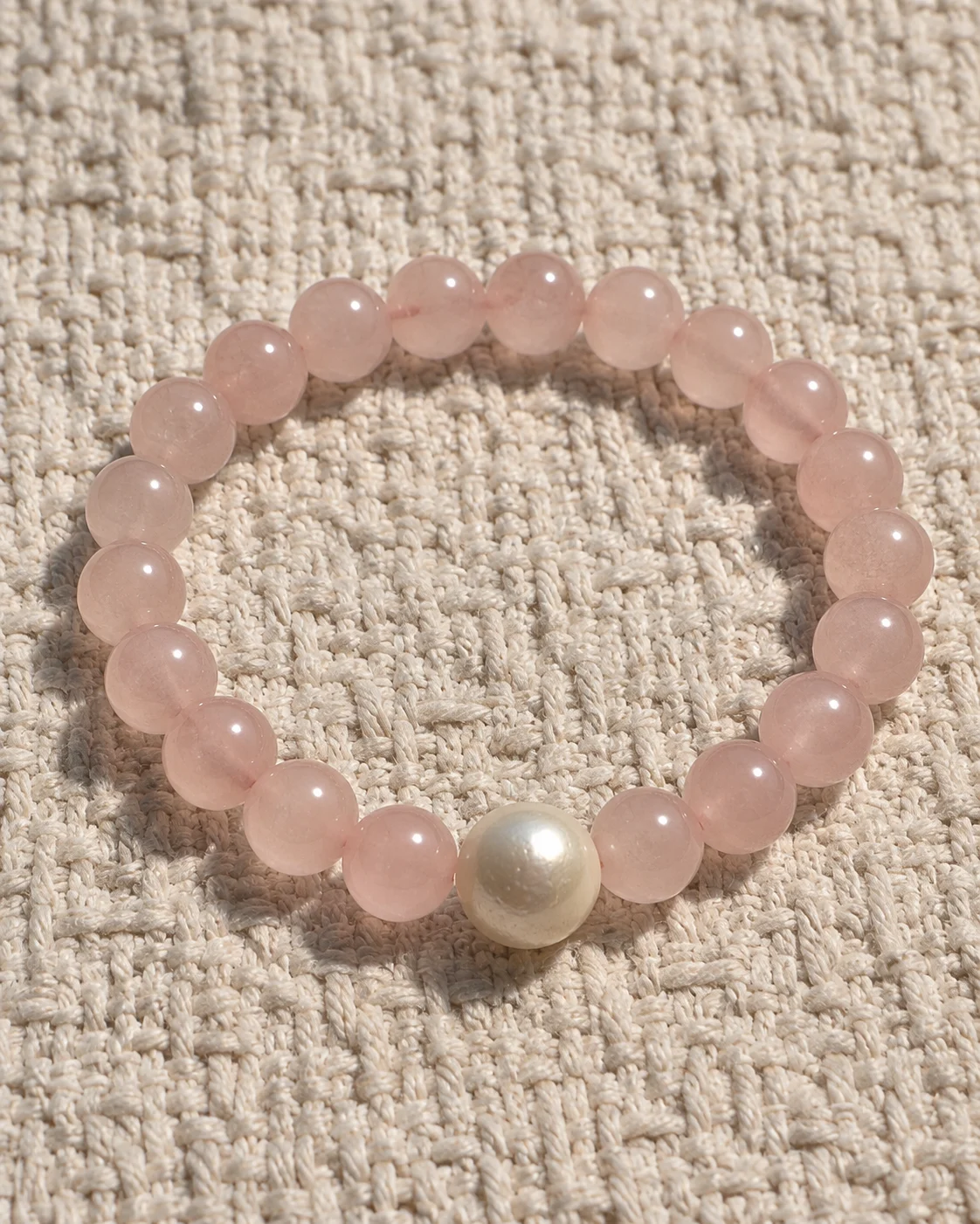 Blush Veil rose quartz bracelet with a single freshwater pearl on textured linen
